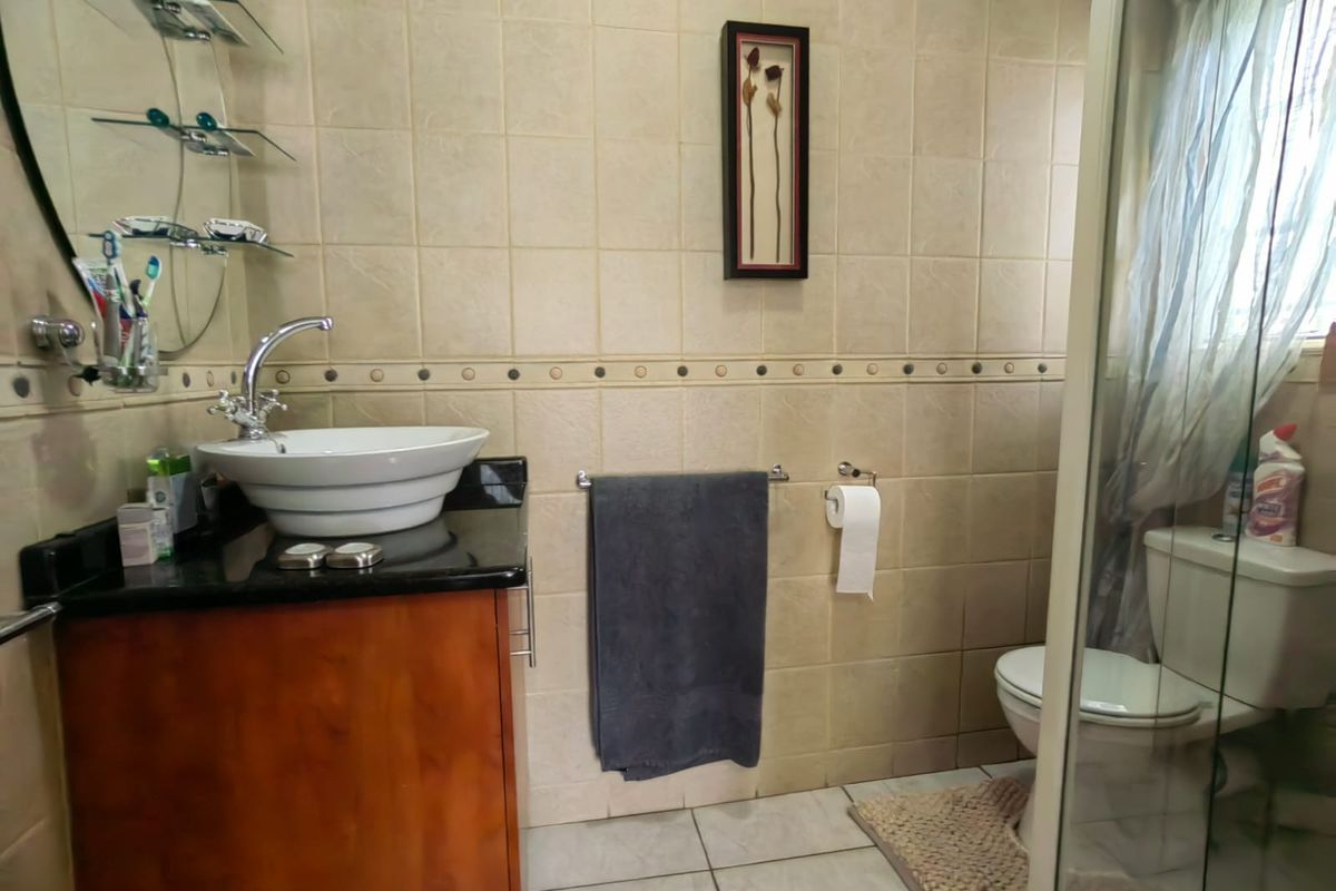 A functional bathroom featuring a vessel sink on a granite vanity, tiled walls, and a glass-enclosed shower area.