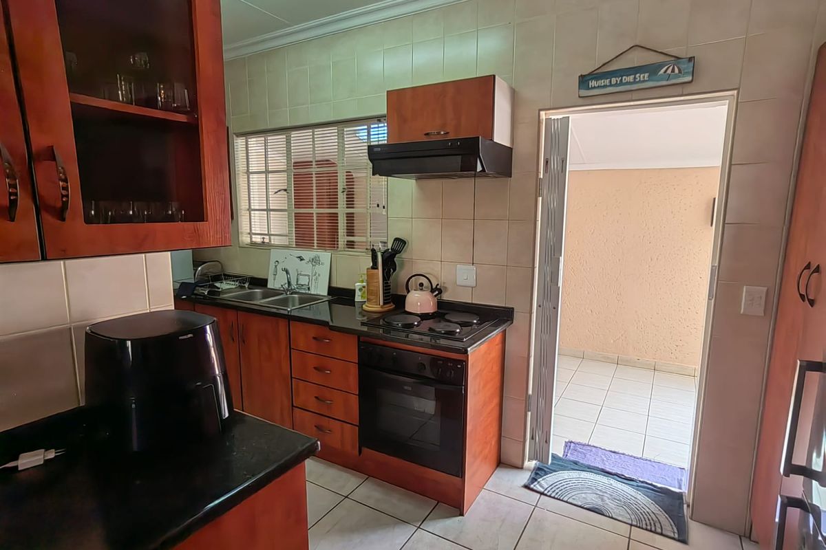 A functional kitchen featuring wood-finish cabinetry, dark countertops, integrated oven and hob, and tiled splashbacks, with direct access to an outdoor patio area.