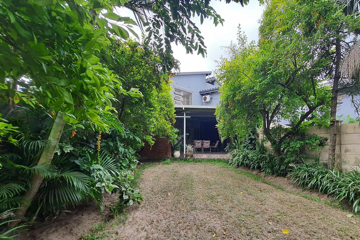 Rear view of the townhouse featuring a covered patio area, established garden with mature trees, and a concrete boundary wall.