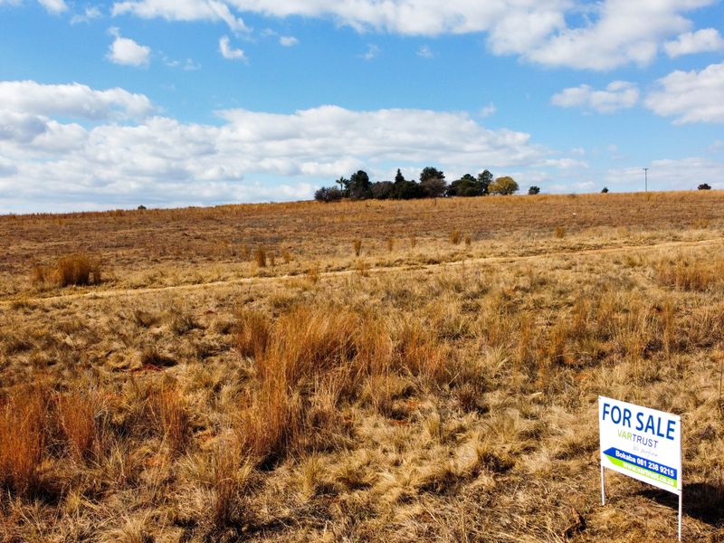 A wide-angle view of a large, undeveloped residential plot of land featuring natural grass coverage and a for-sale sign.