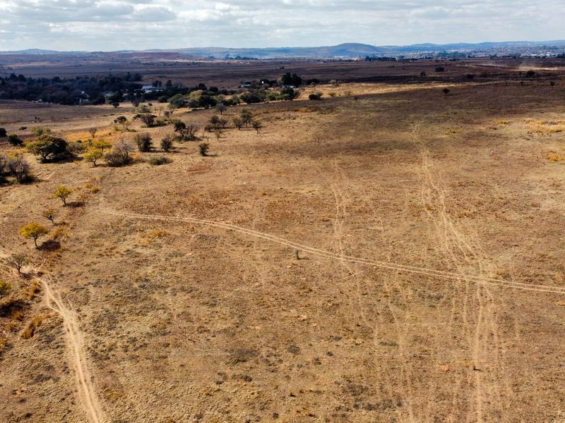 An aerial view of a large, undeveloped residential plot featuring natural dry grassland and scattered indigenous trees.