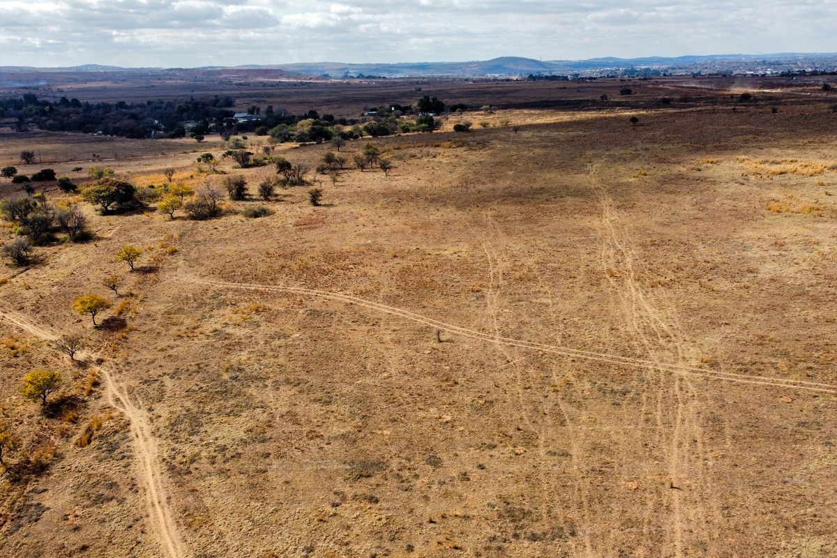 An aerial view of a large, undeveloped residential plot featuring natural dry grassland and scattered indigenous trees.