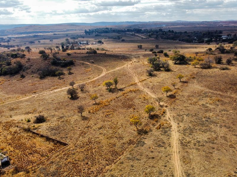 Aerial view of expansive vacant residential land featuring natural vegetation, dirt access tracks, and the remains of a small derelict structure.