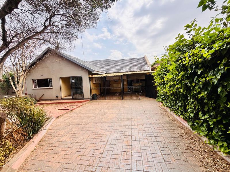 Front exterior view of the house featuring a paved driveway, covered carport area, and established garden surroundings.