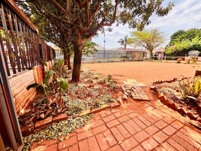 A spacious backyard area featuring a brick-paved section, mature trees, and perimeter metal fencing, offering potential for landscaping and outdoor development.