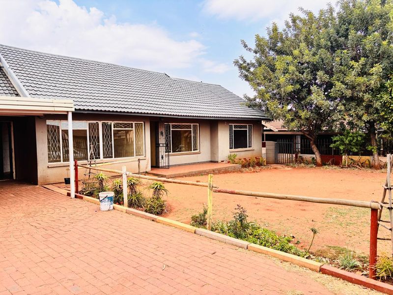 A single-story residential home featuring a tiled roof, paved driveway, and a spacious front garden area with established trees.