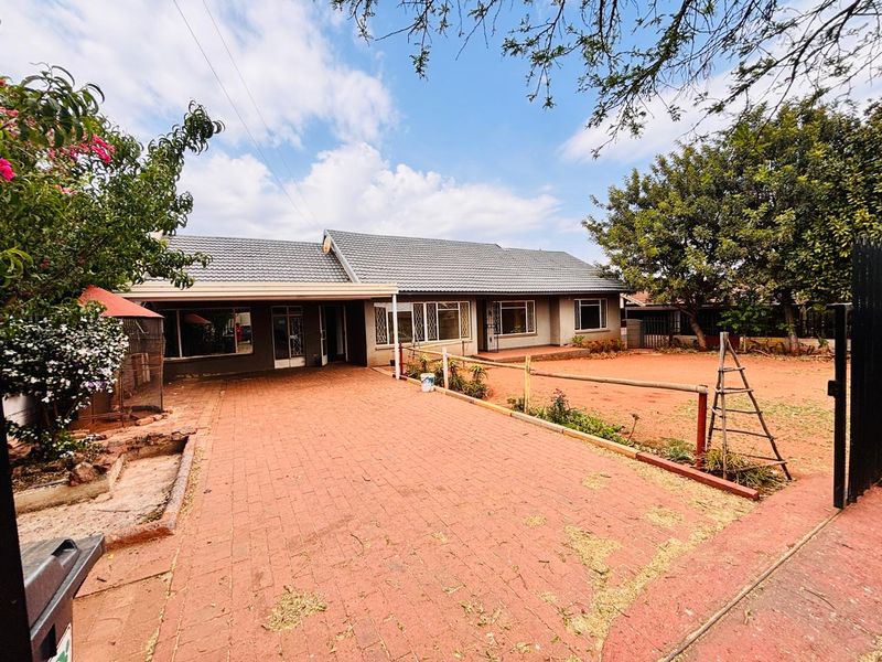 Front view of the house featuring a paved driveway, tiled roof, and a spacious yard area with established trees.