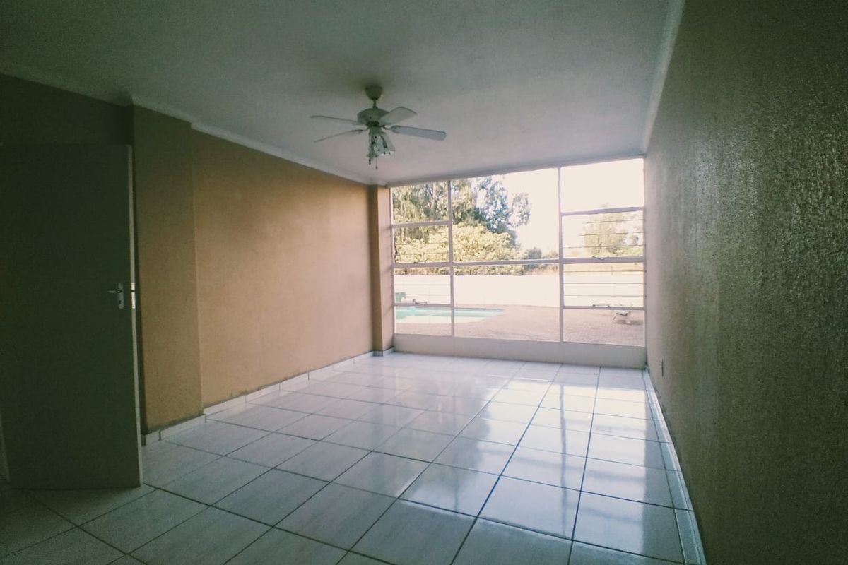 An empty living room featuring tiled flooring, a ceiling fan, and large windows providing natural light and a view of the outdoor area.