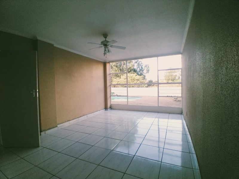 An empty living room featuring tiled flooring, a ceiling fan, and large windows providing natural light and a view of the outdoor area.