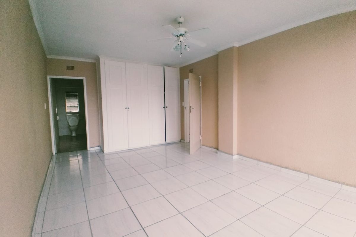 An empty bedroom featuring tiled flooring, built-in cupboards, and a ceiling fan, with an adjacent view into a bathroom.