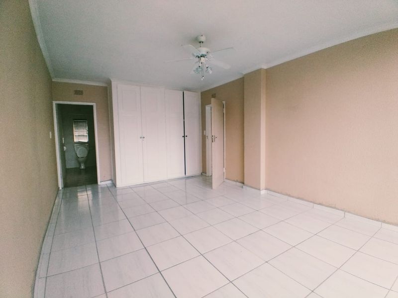An empty bedroom featuring tiled flooring, built-in cupboards, and a ceiling fan, with an adjacent view into a bathroom.