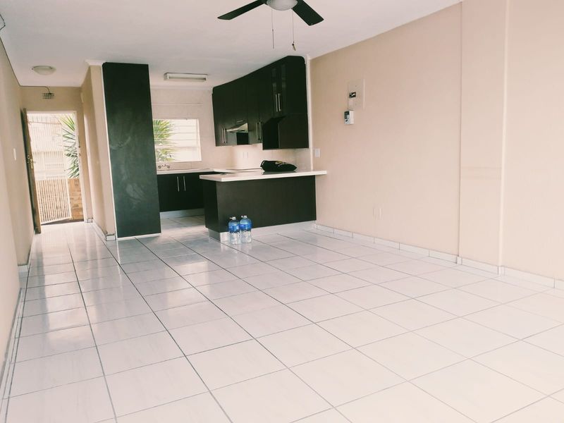Open plan living area featuring tiled flooring, a ceiling fan, and a compact kitchen with dark wood cabinetry and a breakfast bar.