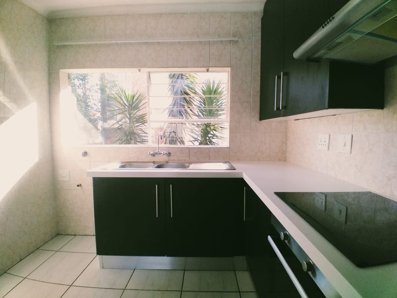 A functional kitchen featuring dark cabinetry, a double sink, integrated electric hob, oven, and extractor fan with tiled finishes throughout.