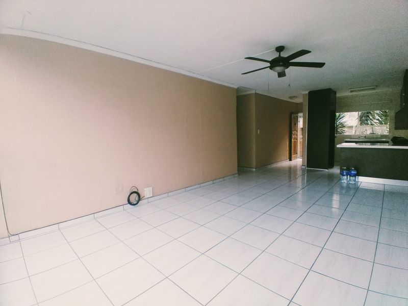 Spacious open-plan living area featuring neutral walls, tiled flooring, and a ceiling fan, seamlessly flowing into the adjacent kitchen space.