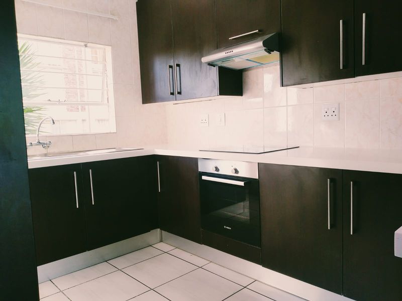A modern, well-maintained kitchen featuring dark wood cabinetry, white stone countertops, built-in oven, electric hob, and a stainless steel sink.