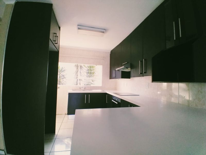 A clean, modern kitchen featuring dark cabinetry, light stone countertops, integrated appliances, and tiled flooring, offering a functional and well-maintained workspace.