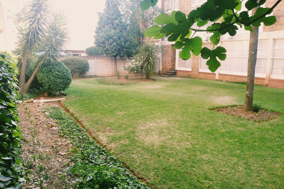 A private rear garden area featuring a lawn, mature trees, and a precast concrete boundary wall adjacent to the apartment building facade.