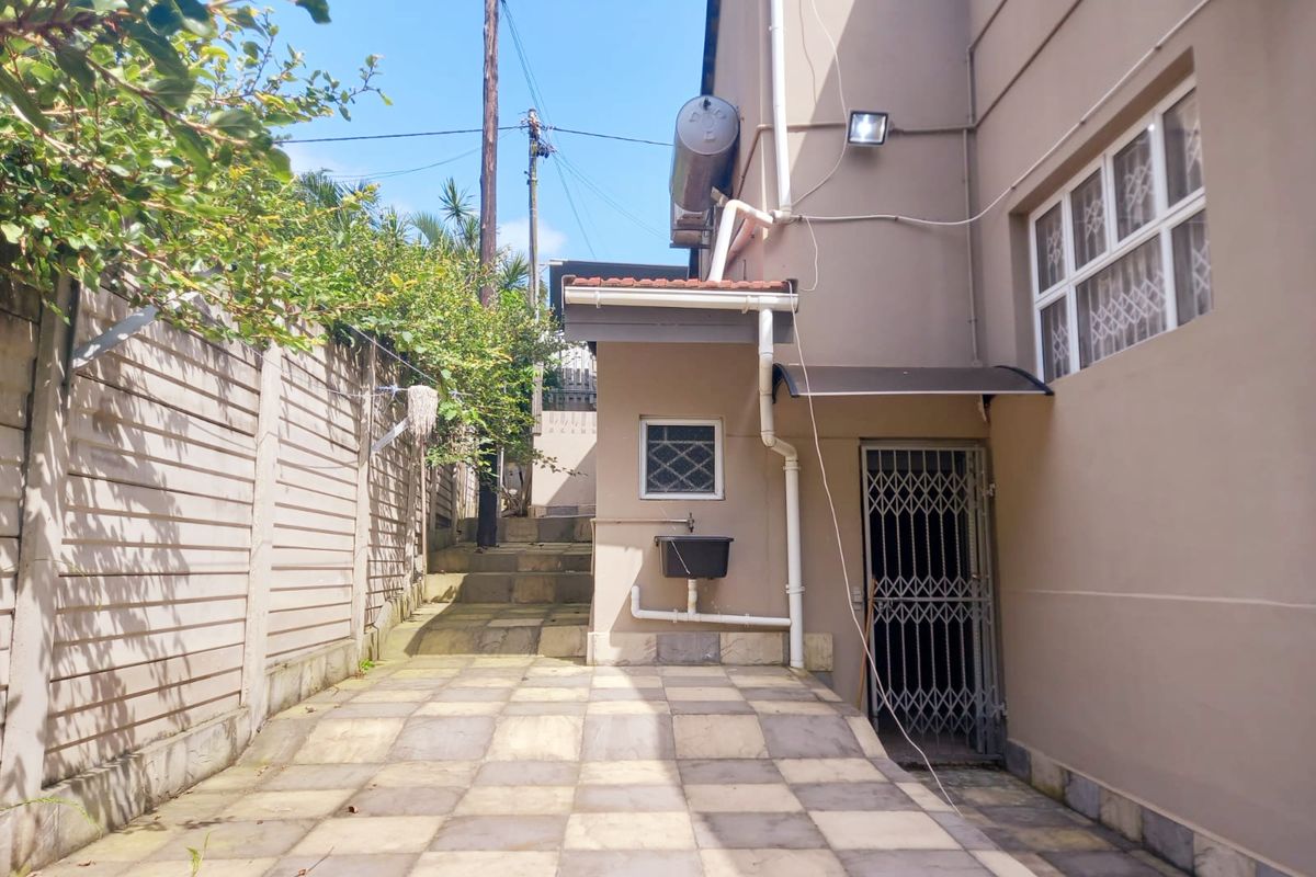 A paved rear exterior area featuring a security gate, external wall-mounted basin, and steps leading to the upper garden level.