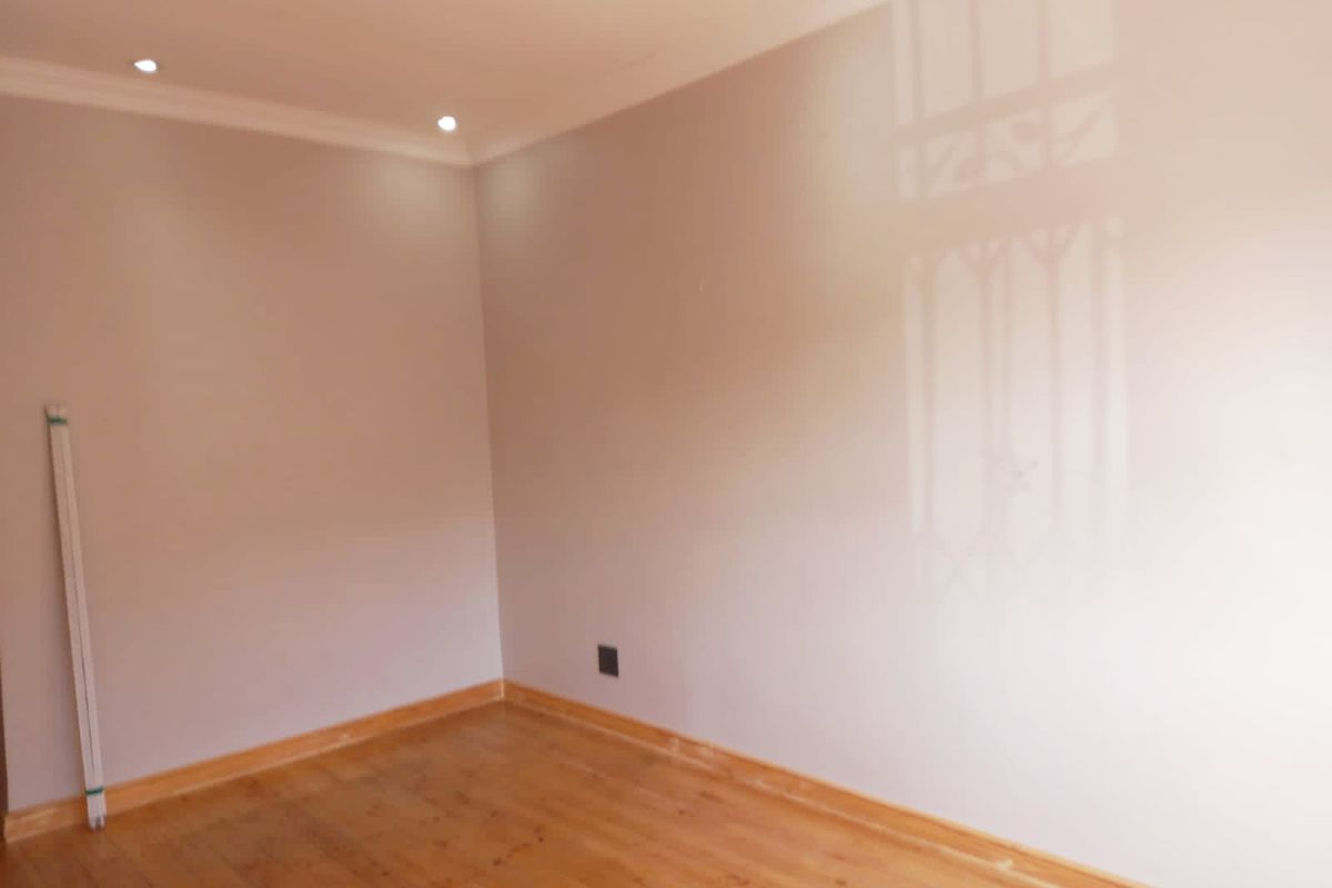 An empty bedroom featuring polished timber flooring, recessed downlighting, and neutral wall finishes.