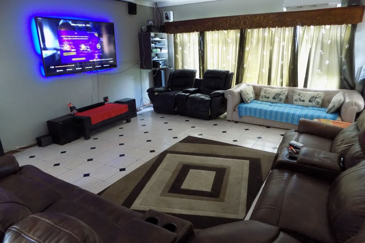 A spacious living room featuring tiled flooring, a wall-mounted air conditioning unit, and built-in shelving, providing a functional space for relaxation and entertainment.