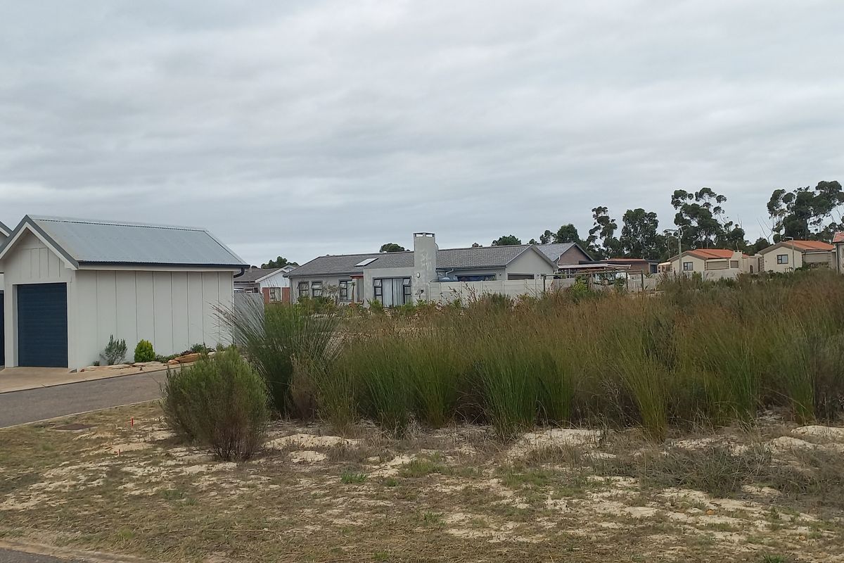 A view of a vacant residential plot adjacent to an existing modern home with a garage and paved driveway.