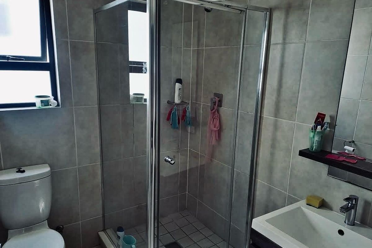 A functional bathroom featuring a glass-enclosed shower, a modern vanity with a basin, and a standard toilet, finished with neutral wall tiles.