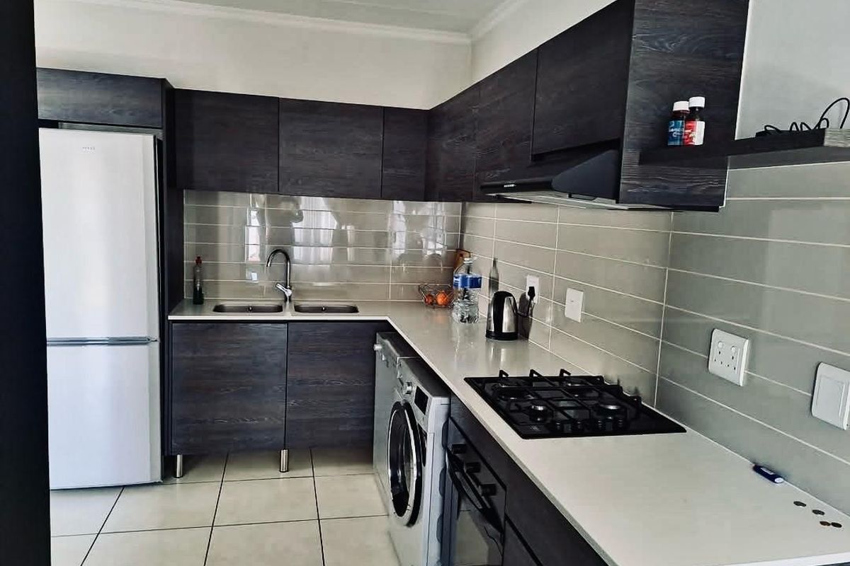 Modern kitchen featuring dark wood-grain cabinetry, stone countertops, integrated gas hob, built-in oven, extractor fan, and tiled splashback.