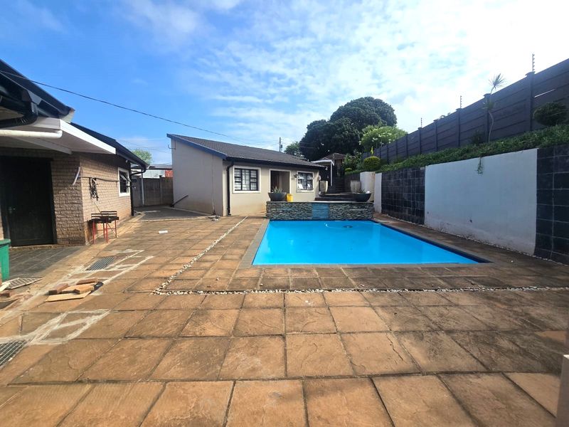 Outdoor pool area featuring a paved patio, a stone-clad water feature, and secure perimeter walling with electric fencing.