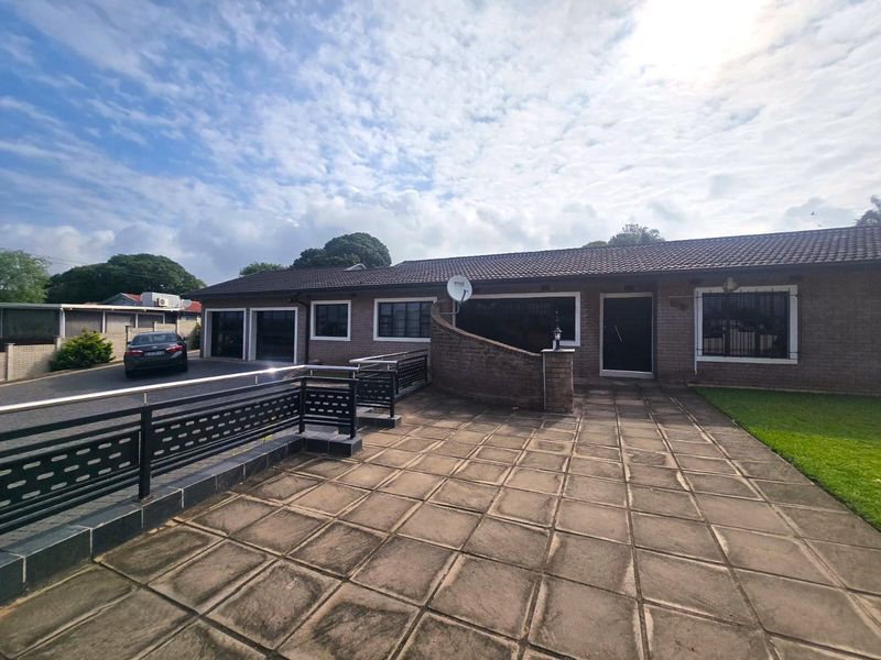 Front exterior view of a brick house featuring a paved patio area, double garage, and secure metal fencing.