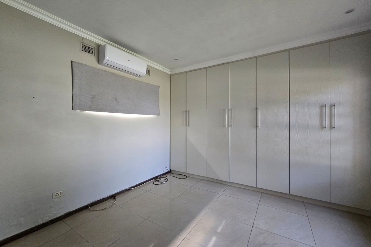 A spacious, empty bedroom featuring neutral tiled flooring, extensive built-in cabinetry, and a wall-mounted split-system air conditioning unit.