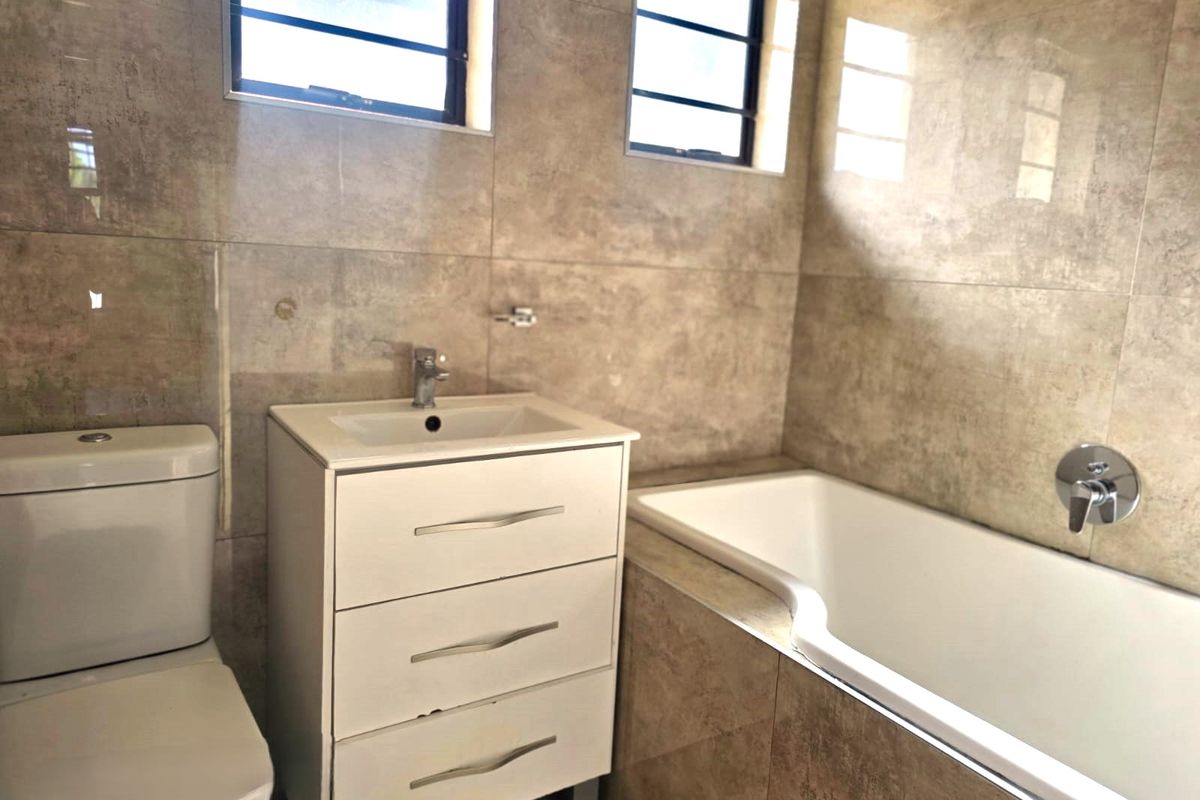 A modern bathroom featuring tiled walls, a white vanity cabinet with basin, a standard toilet, and a built-in bathtub with wall-mounted fixtures.