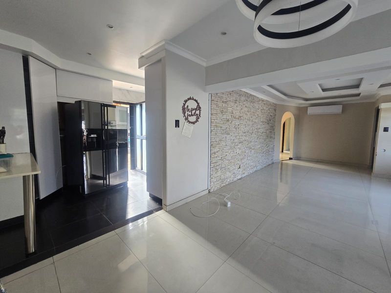 Spacious open-plan living area featuring a textured stone feature wall, modern recessed ceiling lighting, and polished porcelain floor tiles throughout.