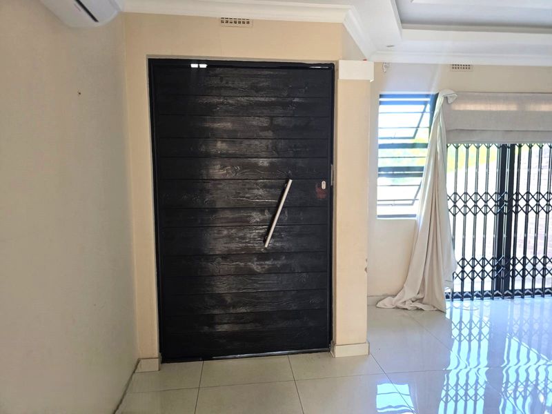 Entrance area featuring tiled flooring, a modern dark wood-look door, security gate, and recessed ceiling detail.