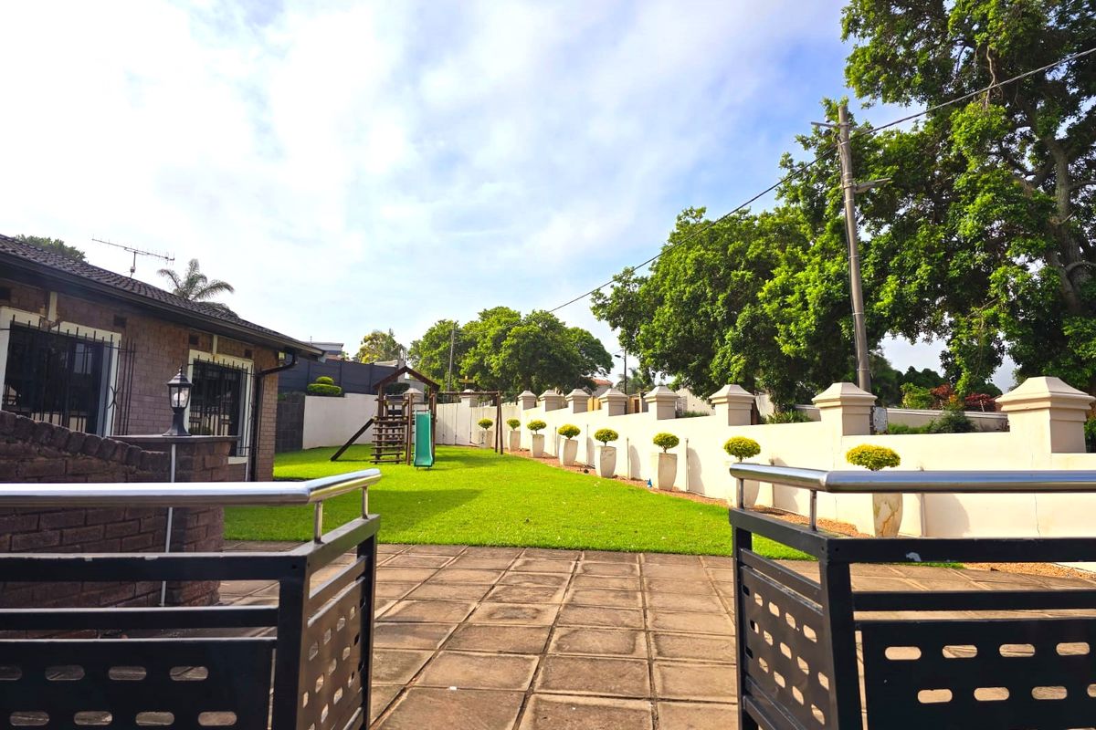 A well-maintained rear garden featuring a paved patio area, metal balustrades, and a manicured lawn enclosed by a perimeter wall.