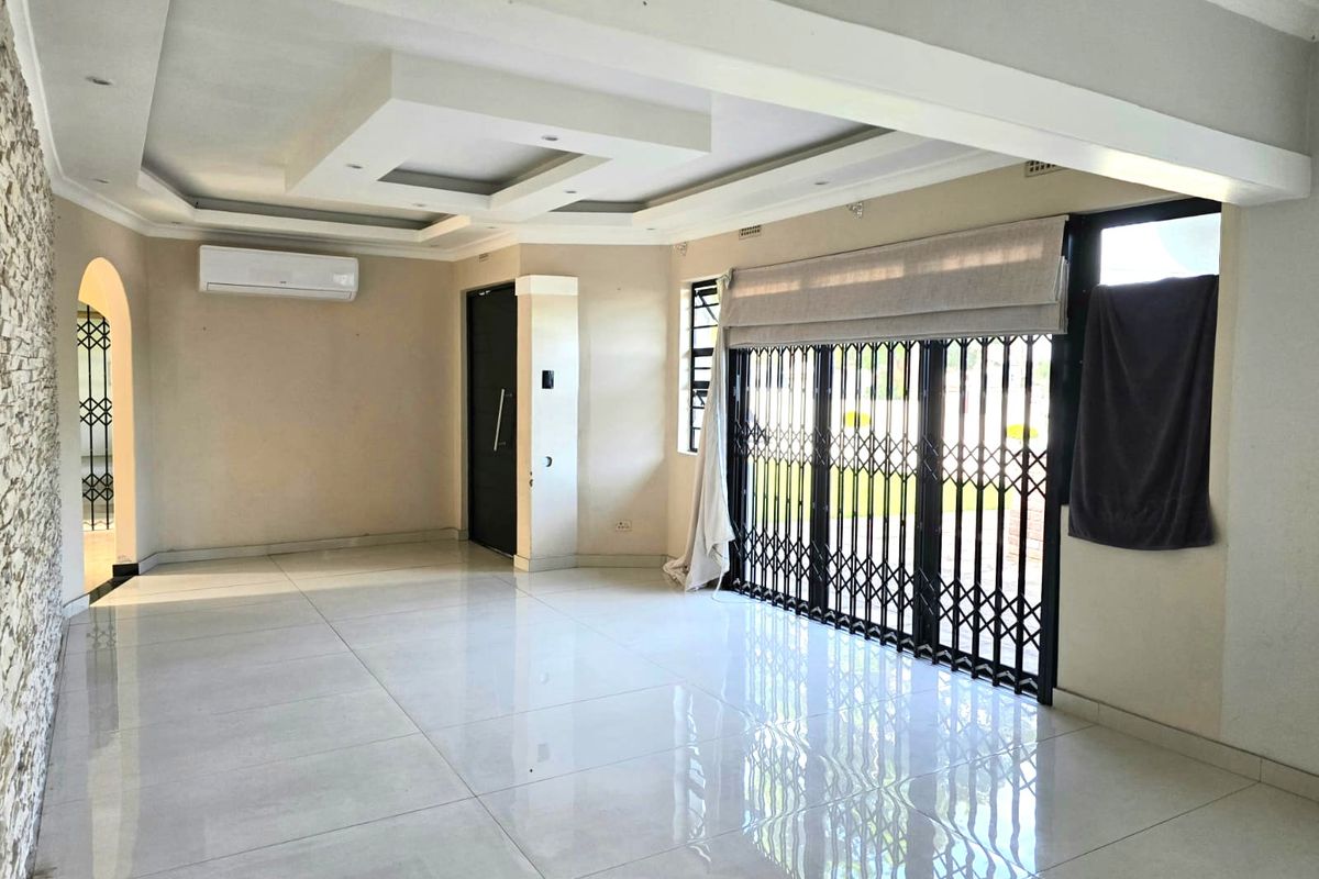 Spacious, empty living area featuring polished porcelain floor tiles, a modern recessed ceiling, and a stone feature wall with an installed air conditioning unit.