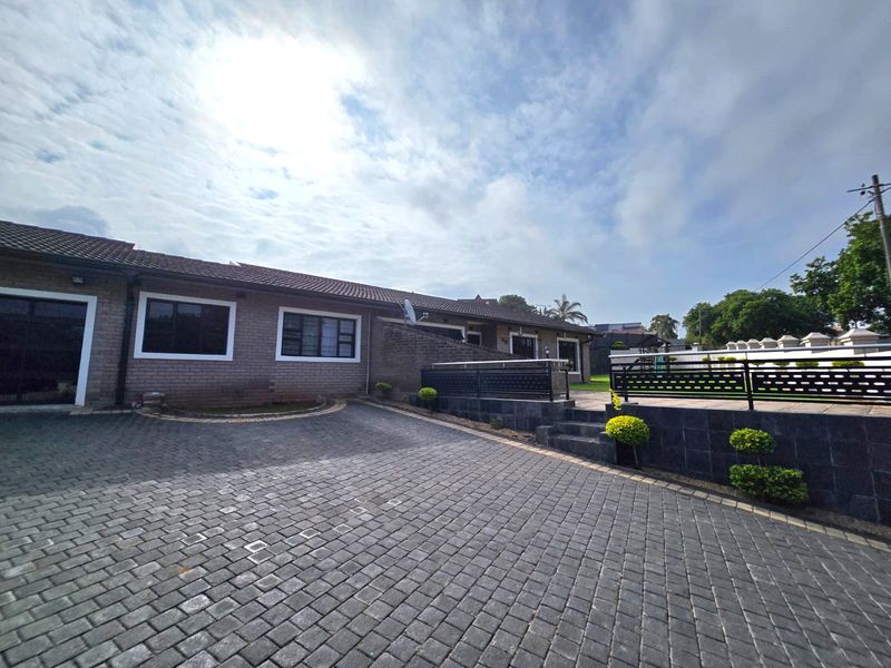 Front exterior view of a brick house featuring a spacious paved driveway, retaining walls, and modern metal balustrades.