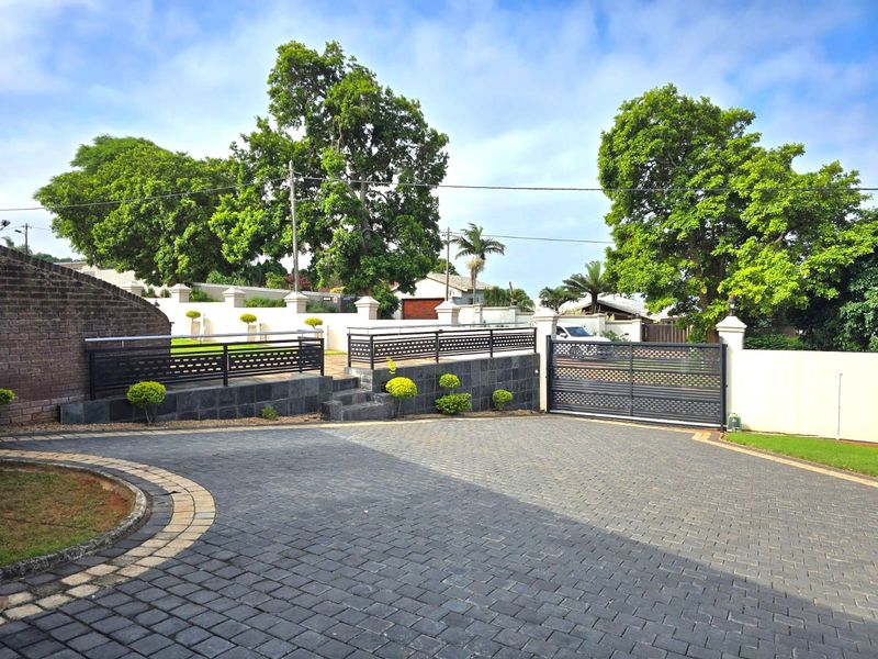A well-maintained front entrance featuring a paved driveway, secure metal gate, and stone-clad retaining walls with integrated perimeter fencing.