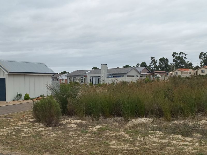 A view of a vacant residential plot adjacent to an existing modern home with a garage and paved driveway.