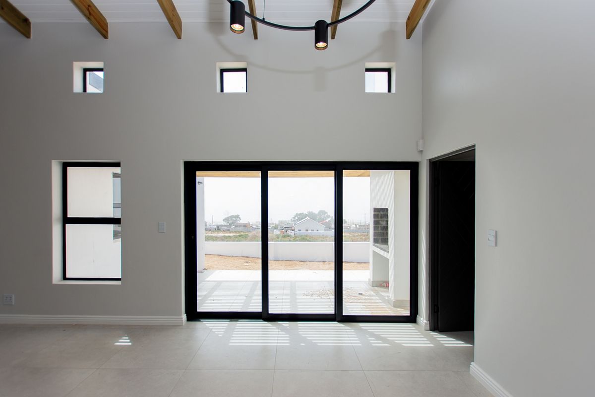 Spacious living area featuring high ceilings with exposed timber beams, modern tiled flooring, and large black aluminium sliding doors opening to an outdoor patio.