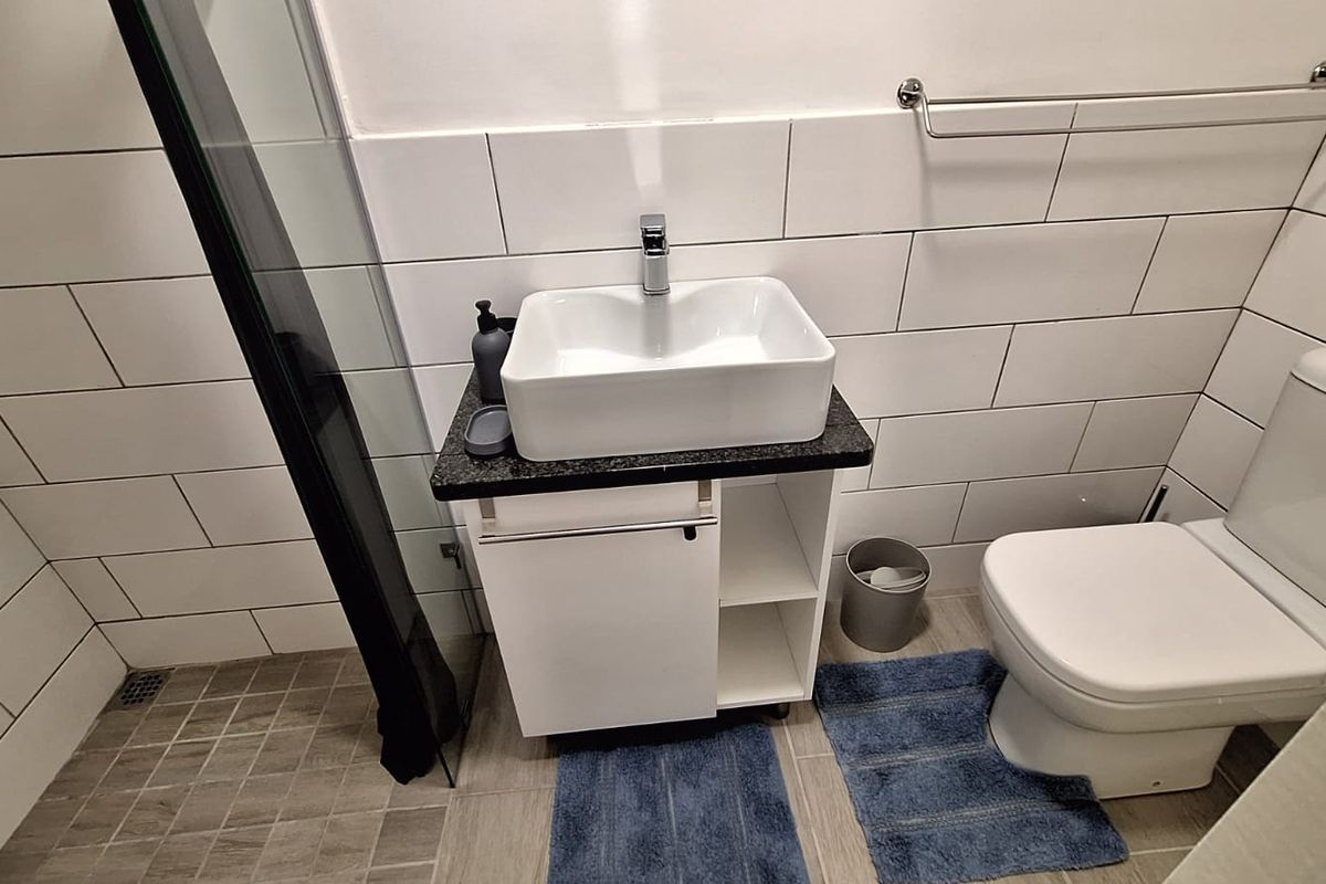 Modern bathroom featuring a vessel sink with vanity cabinet, a toilet, and a shower enclosure with white subway wall tiling.