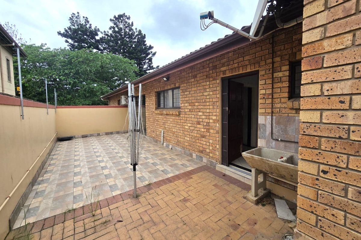 Rear exterior area featuring a combination of tiled and paved patio space, a brick facade, and a built-in concrete laundry sink.