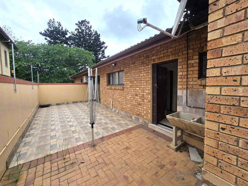 Rear exterior area featuring a combination of tiled and paved patio space, a brick facade, and a built-in concrete laundry sink.