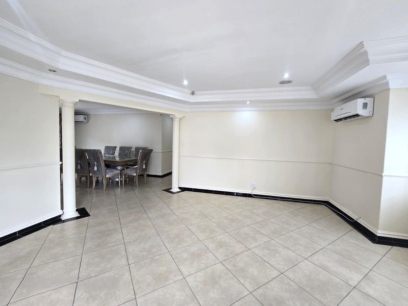 Spacious open-plan living and dining area featuring tiled floors, decorative columns, recessed ceiling details, and wall-mounted air conditioning units.