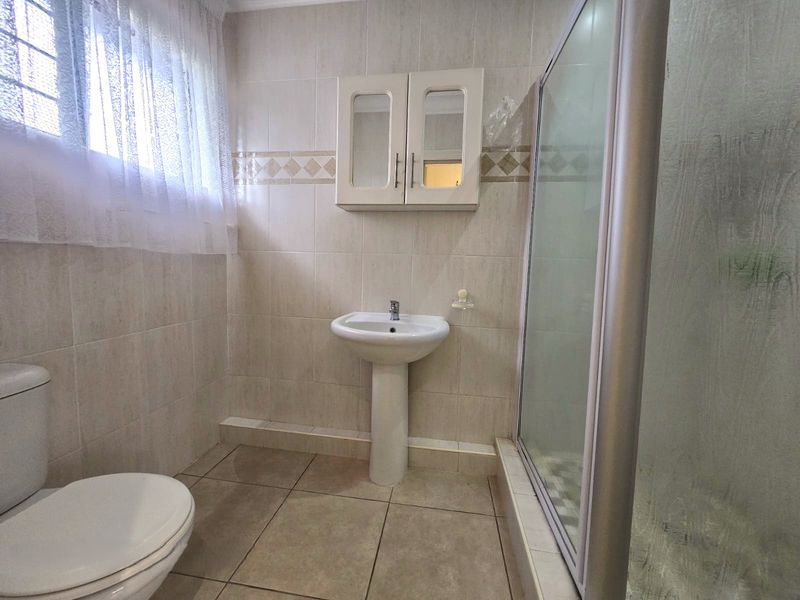 A functional bathroom featuring a pedestal sink, a shower enclosure, a toilet, and a wall-mounted medicine cabinet with neutral wall and floor tiling.