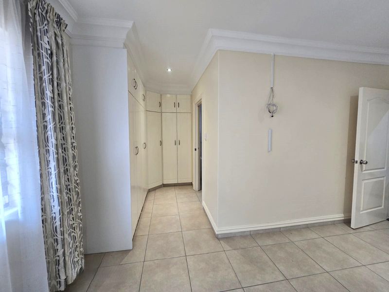 A spacious bedroom featuring neutral tiled flooring, extensive built-in cupboard storage, and decorative ceiling cornicing.
