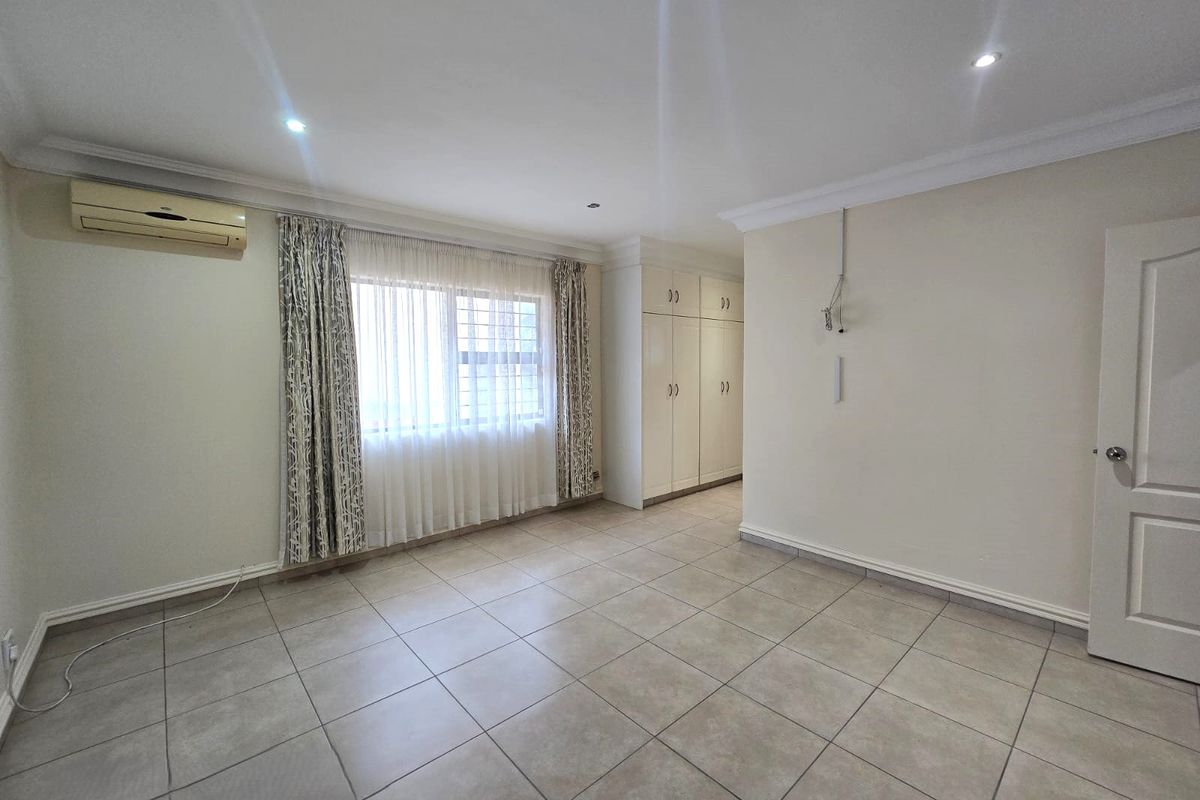 A spacious, neutral bedroom featuring tiled flooring, built-in cupboards, recessed lighting, and an installed air conditioning unit.