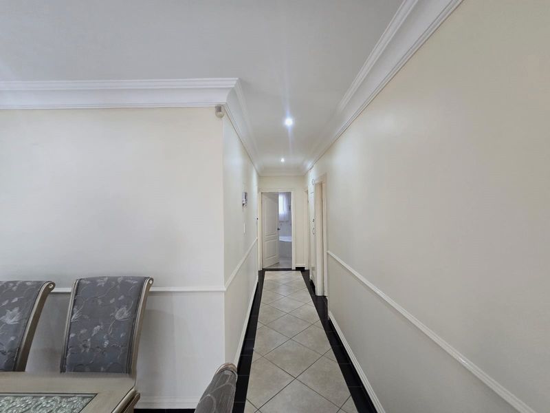A clean, well-lit hallway featuring crown molding, chair rail detailing, and neutral tiled flooring, providing access to adjacent rooms.
