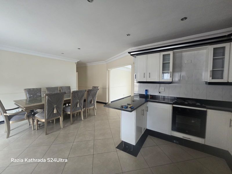 Open-plan kitchen and dining area featuring white cabinetry, granite countertops, built-in oven, gas hob, and tiled flooring throughout.