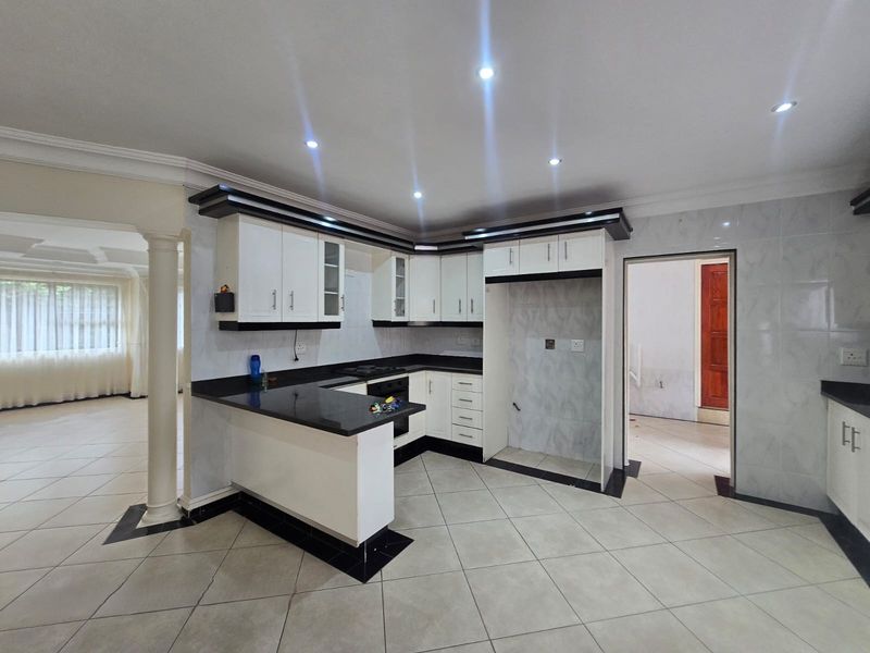 A modern, well-lit kitchen featuring white cabinetry, black granite countertops, a breakfast bar, and tiled flooring, offering a clean and functional workspace.