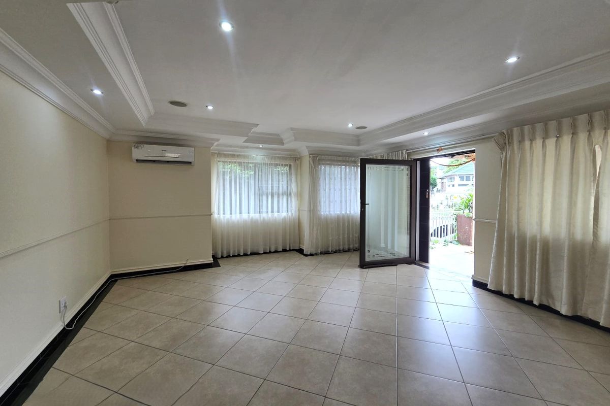 Spacious, light-filled living area featuring neutral tiled flooring, recessed ceiling with cove lighting, and a split-system air conditioner, opening directly to an outdoor space.